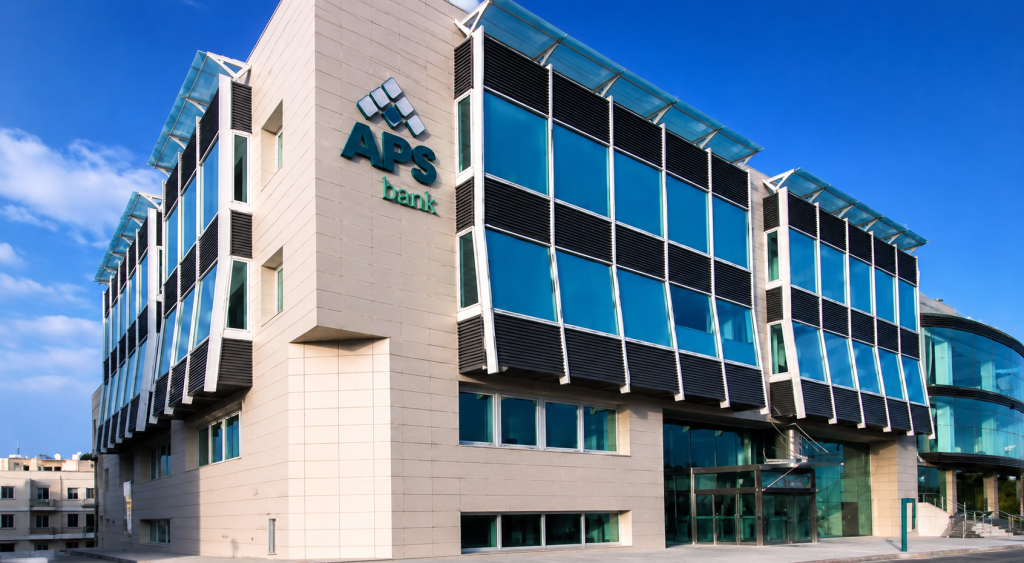 APS Bank logo displayed on a modern office building with blue-tinted glass windows.
